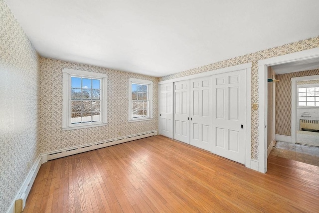 unfurnished bedroom with a closet, baseboard heating, and light hardwood / wood-style flooring