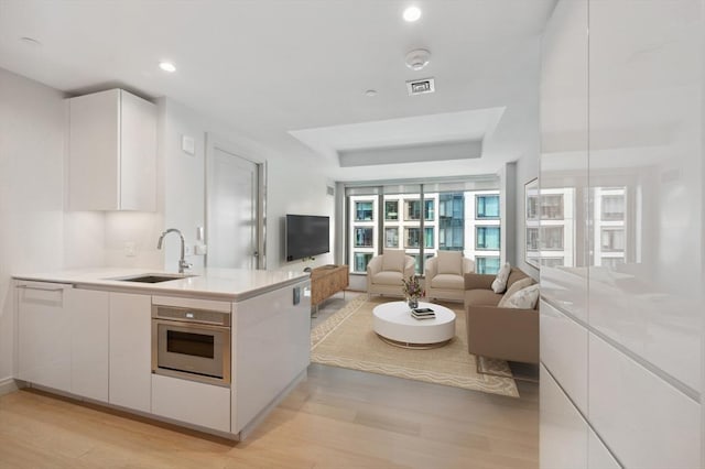 kitchen with stainless steel oven, sink, white cabinets, and light hardwood / wood-style floors