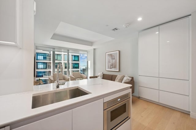 kitchen featuring a raised ceiling, sink, white cabinets, and light hardwood / wood-style floors