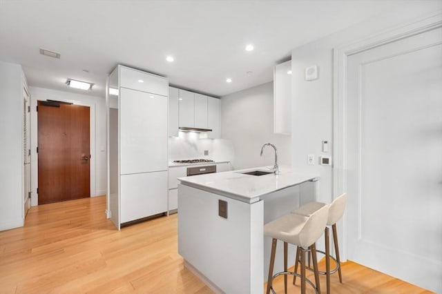 kitchen featuring kitchen peninsula, a breakfast bar, stainless steel gas cooktop, sink, and white cabinets