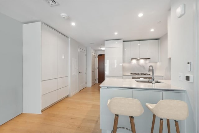 kitchen featuring white cabinetry, sink, kitchen peninsula, light hardwood / wood-style floors, and a breakfast bar area