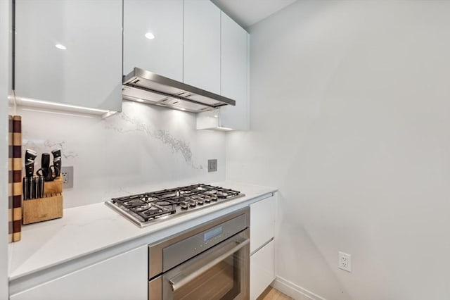 kitchen with ventilation hood, stainless steel appliances, white cabinetry, and light stone counters