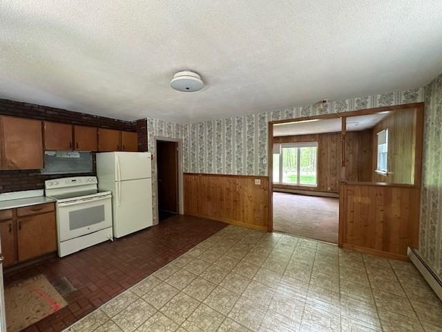 kitchen with white appliances, a baseboard heating unit, wallpapered walls, a wainscoted wall, and wooden walls