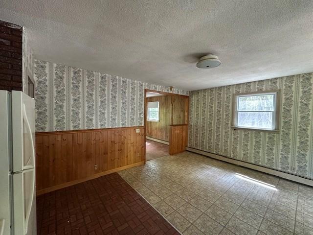 unfurnished room with wallpapered walls, wainscoting, a baseboard heating unit, a textured ceiling, and a baseboard radiator