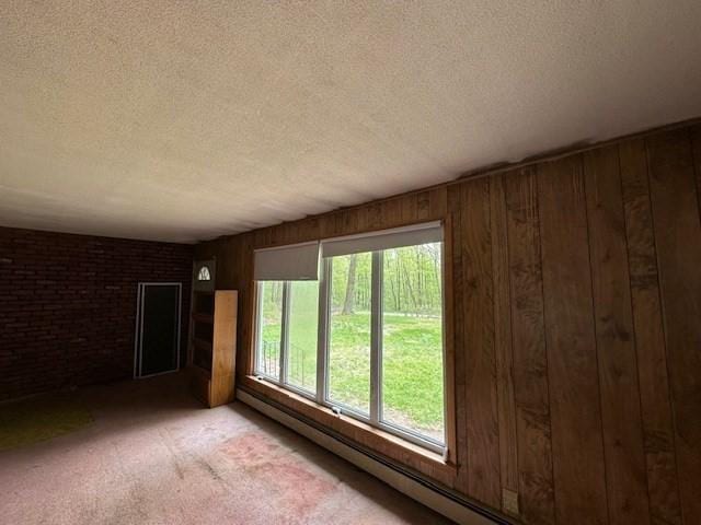 spare room featuring a textured ceiling, wood walls, a baseboard radiator, light carpet, and brick wall