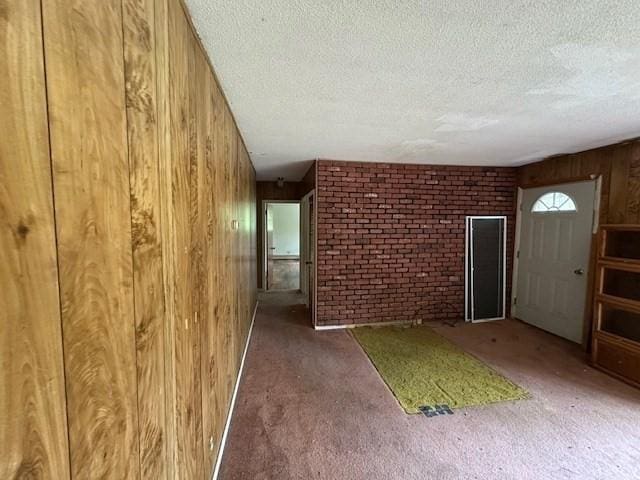 unfurnished living room with wooden walls, a textured ceiling, brick wall, and carpet
