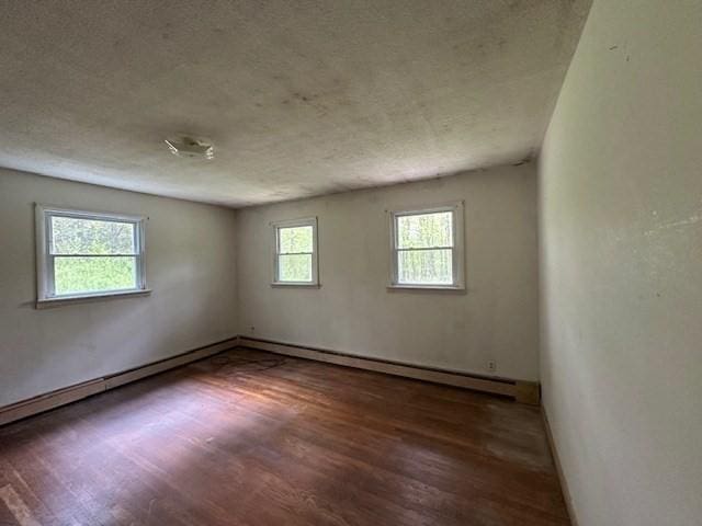 unfurnished room featuring wood finished floors, a textured ceiling, baseboard heating, and baseboards