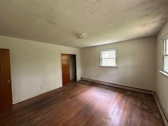unfurnished room with baseboard heating, wood finished floors, a textured ceiling, and baseboards