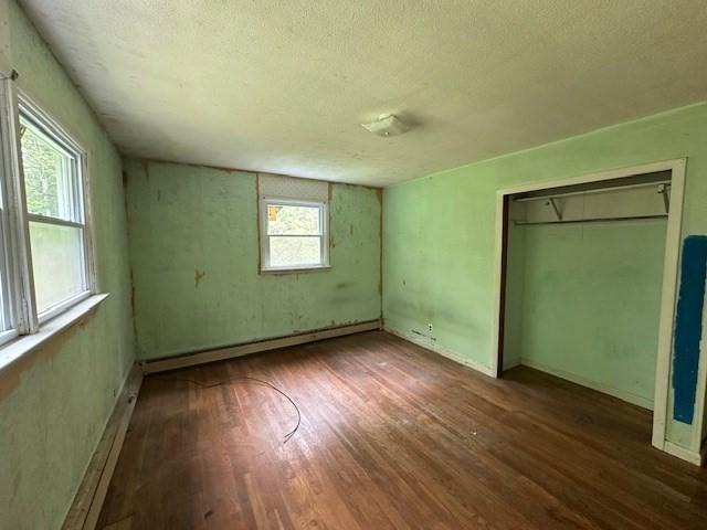unfurnished bedroom featuring wood finished floors, a textured ceiling, baseboard heating, and a closet