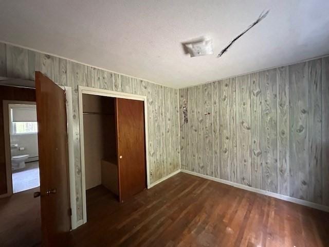 unfurnished bedroom featuring wood finished floors, a closet, baseboards, wood walls, and baseboard heating