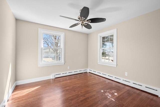 empty room featuring a healthy amount of sunlight, a baseboard heating unit, and wood finished floors