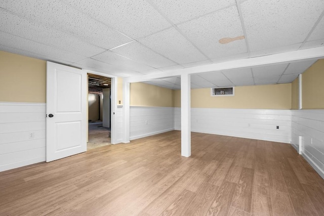 finished basement with a wainscoted wall, a paneled ceiling, and wood finished floors