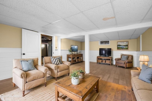 living area with a drop ceiling, light wood-style flooring, and wainscoting