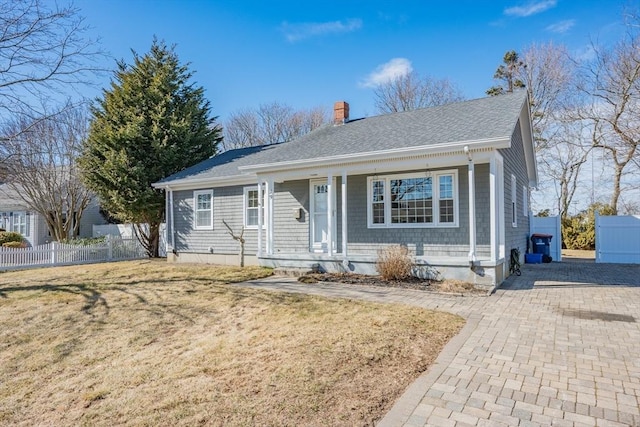 view of front of property featuring a front lawn, fence, roof with shingles, covered porch, and a chimney