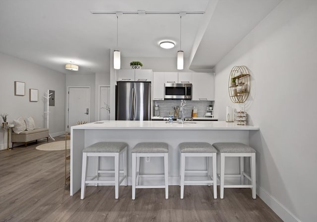 kitchen featuring sink, white cabinetry, kitchen peninsula, stainless steel appliances, and backsplash