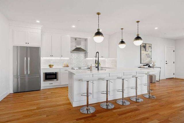 kitchen featuring wall chimney exhaust hood, stainless steel appliances, light wood-style floors, white cabinetry, and a sink