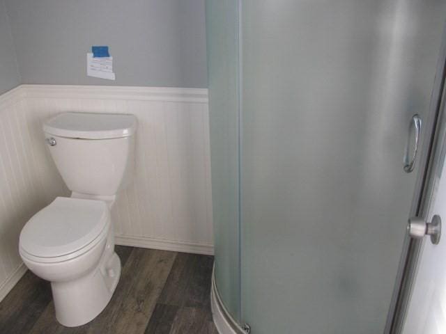 bathroom with an enclosed shower, toilet, and wood-type flooring