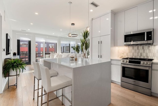 kitchen featuring white cabinetry, hanging light fixtures, light hardwood / wood-style flooring, decorative backsplash, and appliances with stainless steel finishes