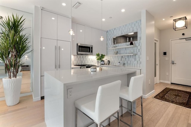 kitchen with backsplash, a breakfast bar, white cabinets, light hardwood / wood-style floors, and hanging light fixtures