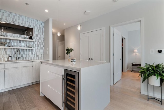 bar featuring light wood-type flooring, sink, white cabinets, wine cooler, and hanging light fixtures