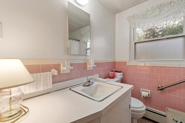 bathroom featuring a baseboard heating unit, toilet, vanity, wainscoting, and tile walls