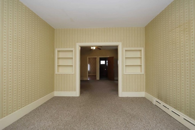 unfurnished room with a baseboard heating unit, built in shelves, ceiling fan, and carpet flooring