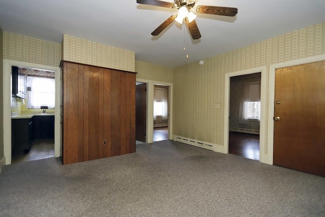 unfurnished bedroom with dark colored carpet, ensuite bathroom, a baseboard heating unit, and ceiling fan