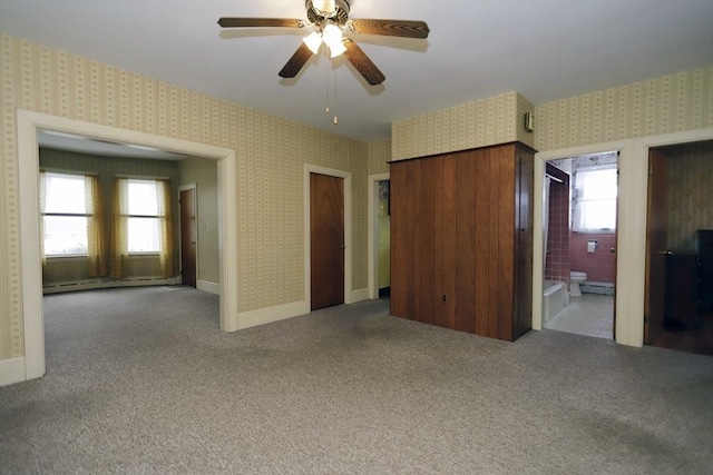 unfurnished bedroom featuring multiple windows, connected bathroom, a baseboard radiator, and ceiling fan