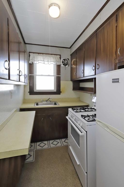 kitchen featuring ornamental molding, dark brown cabinets, sink, and white appliances