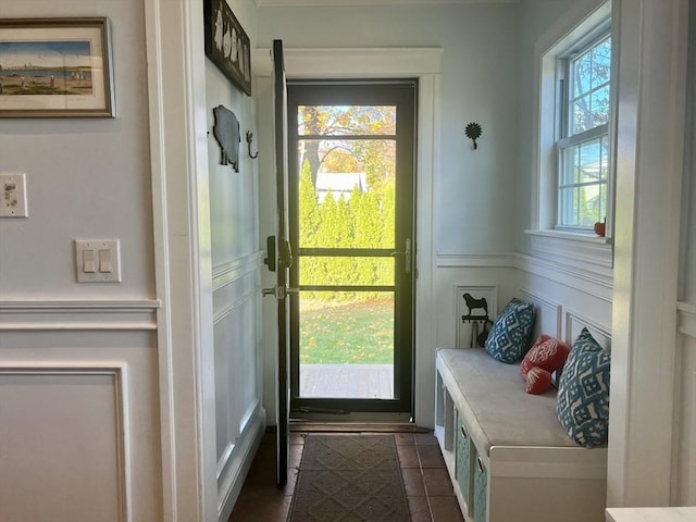 doorway with a healthy amount of sunlight, a wainscoted wall, dark tile patterned floors, and a decorative wall