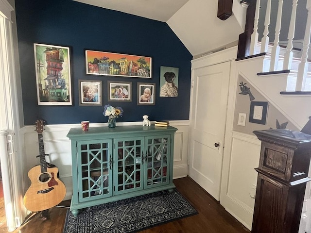 bar featuring lofted ceiling, a decorative wall, wood finished floors, stairs, and wainscoting