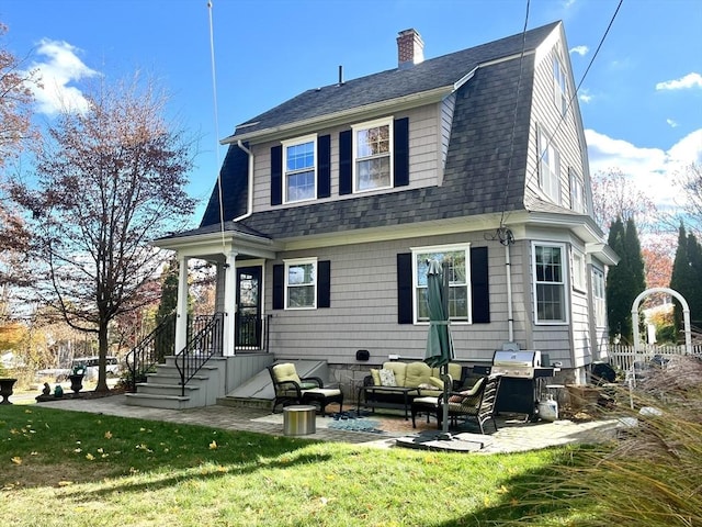 rear view of property featuring a gambrel roof, a chimney, roof with shingles, a yard, and outdoor lounge area