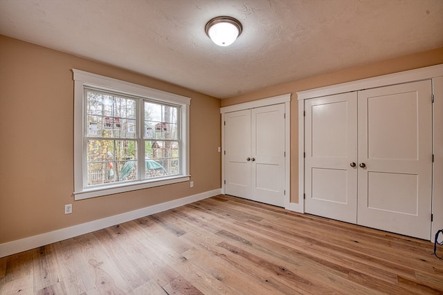 unfurnished bedroom featuring a textured ceiling, light wood-type flooring, and two closets