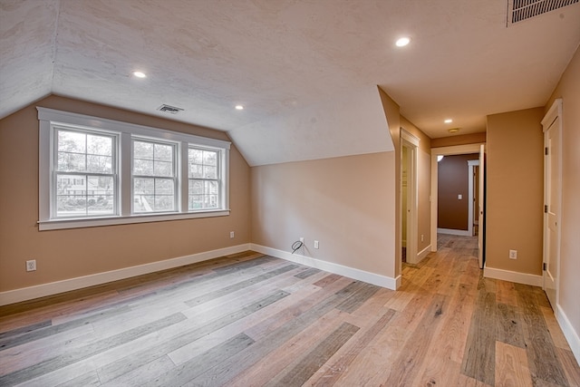 additional living space with vaulted ceiling and light hardwood / wood-style flooring