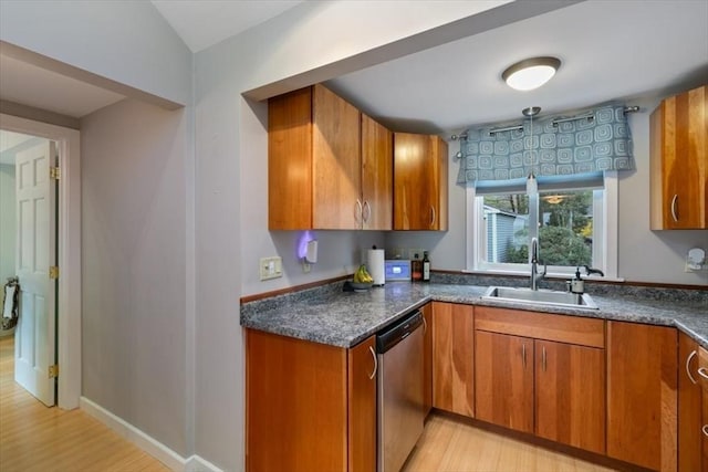 kitchen with dishwasher, a sink, brown cabinets, light wood-type flooring, and dark countertops
