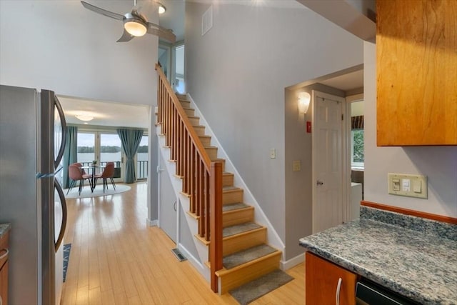 stairway with wood finished floors, baseboards, ceiling fan, and a high ceiling