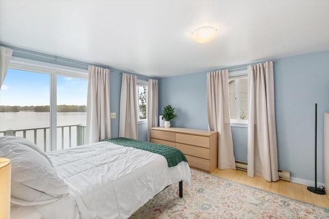 bedroom featuring light wood-type flooring, a baseboard heating unit, a water view, and baseboard heating