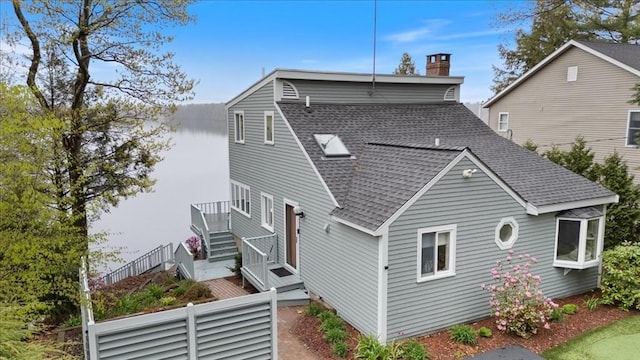 back of house with roof with shingles, a chimney, and stairway