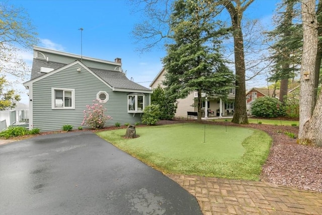 view of front of home with an area to practice putting, a chimney, roof with shingles, and a patio area