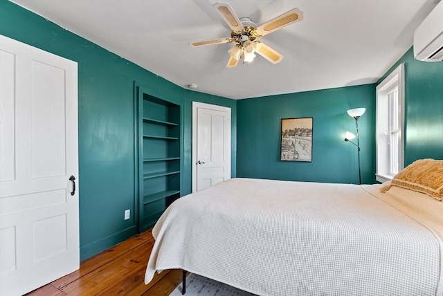 bedroom featuring hardwood / wood-style floors, a ceiling fan, baseboards, and a wall mounted AC