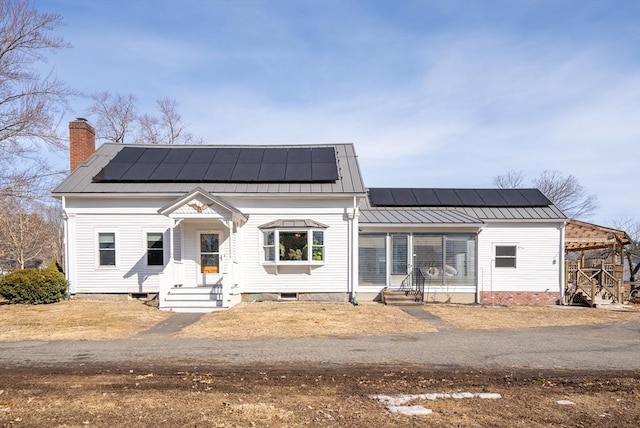 view of front of home with metal roof, solar panels, a chimney, and a standing seam roof