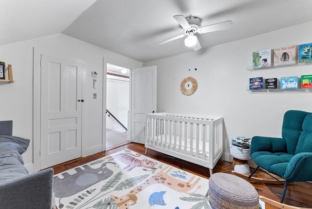 bedroom with vaulted ceiling, a nursery area, ceiling fan, and wood finished floors