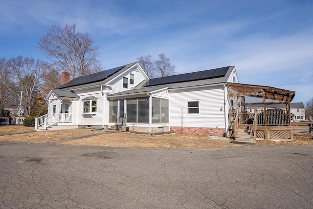 view of front of home with solar panels, a sunroom, and a chimney