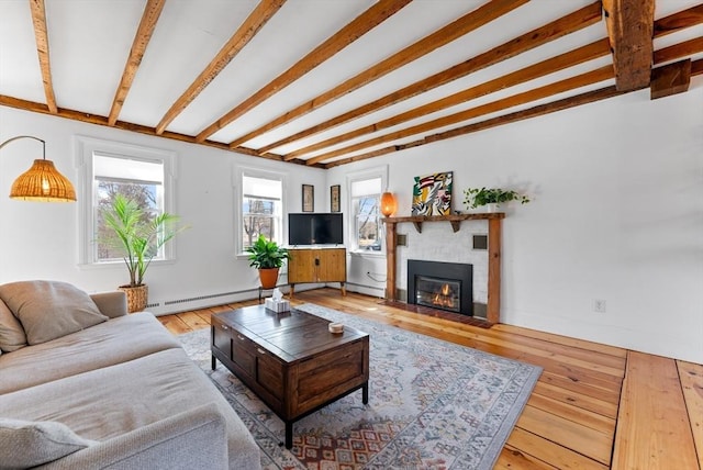 living area featuring hardwood / wood-style floors, beam ceiling, a glass covered fireplace, and a baseboard radiator