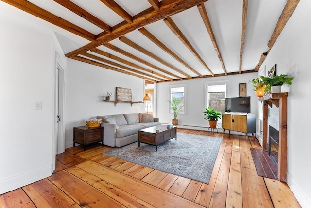 living area with beam ceiling, a fireplace with flush hearth, light wood-style floors, and baseboards