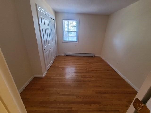 empty room with wood finished floors, baseboards, and a baseboard radiator