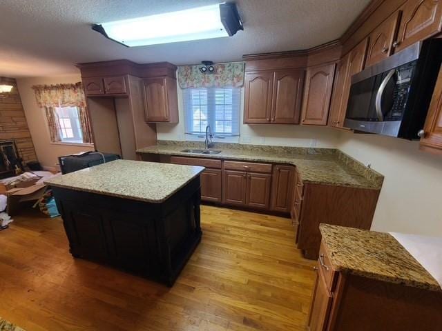 kitchen with stainless steel microwave, a center island, light stone counters, light wood-style floors, and a sink