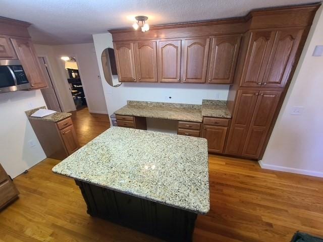 kitchen featuring stainless steel microwave, light stone counters, and light wood-style floors