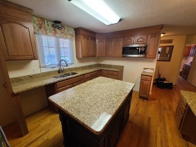 kitchen with a sink, stainless steel microwave, light stone counters, and wood finished floors