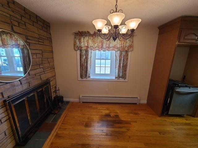 dining room featuring baseboards, a fireplace, light wood-style floors, a baseboard heating unit, and a notable chandelier